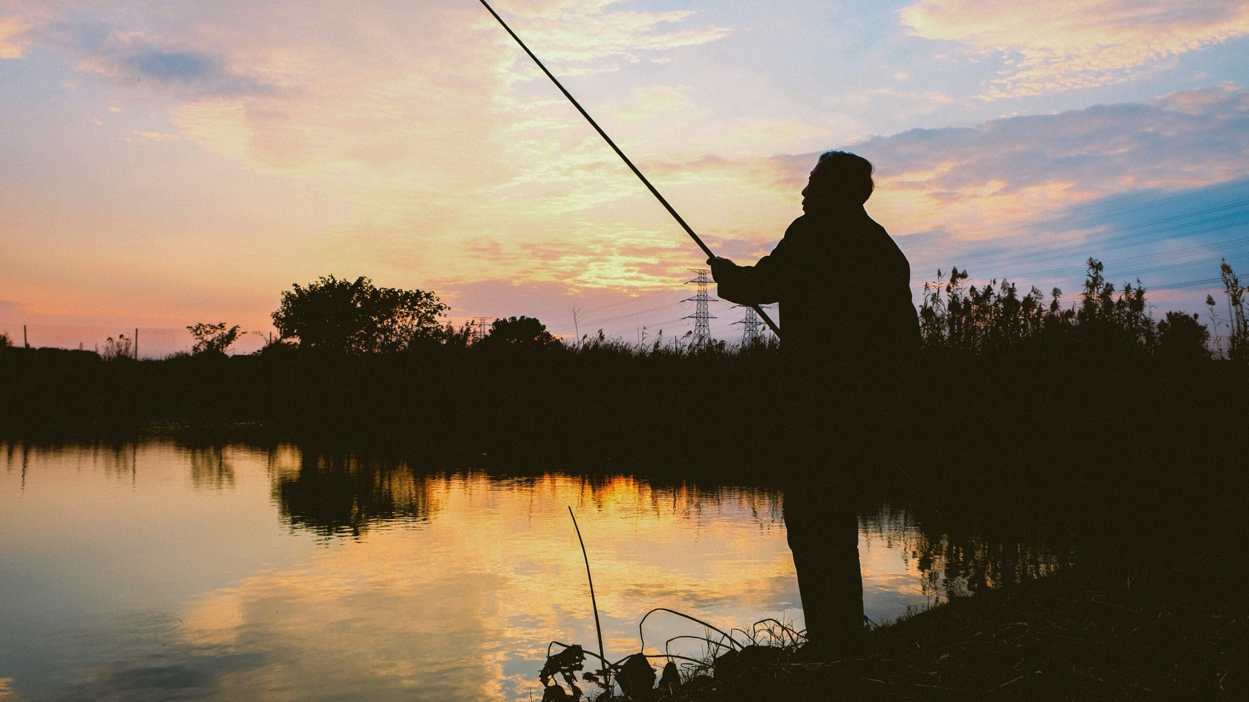 Silhouette of an angler fishing from the bank of a calm lake at golden hour, set within the KG Retreats estate in Rutland